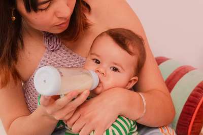 A mother feeding a baby with a bottle on a colorful couch.