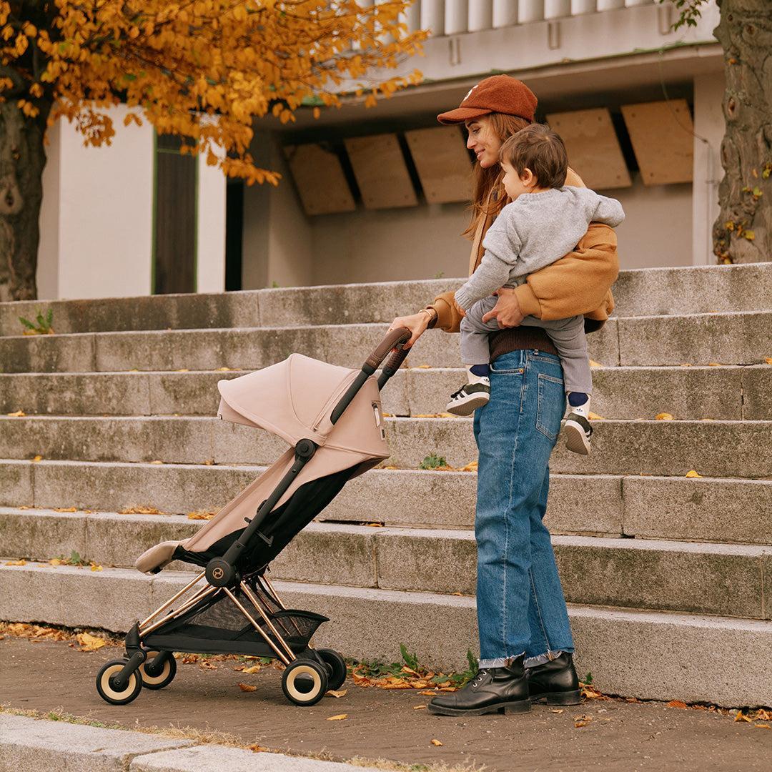 Person holding a child next to a stroller on outdoor steps.