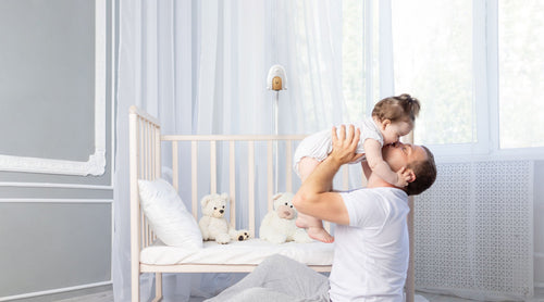 Father lifting daughter in a bright nursery with a crib and toys.