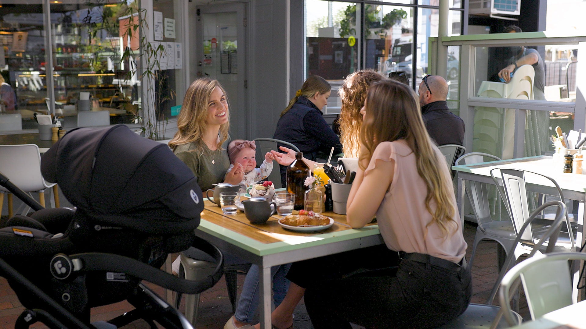 Group of people dining together in a café with a stroller nearby.