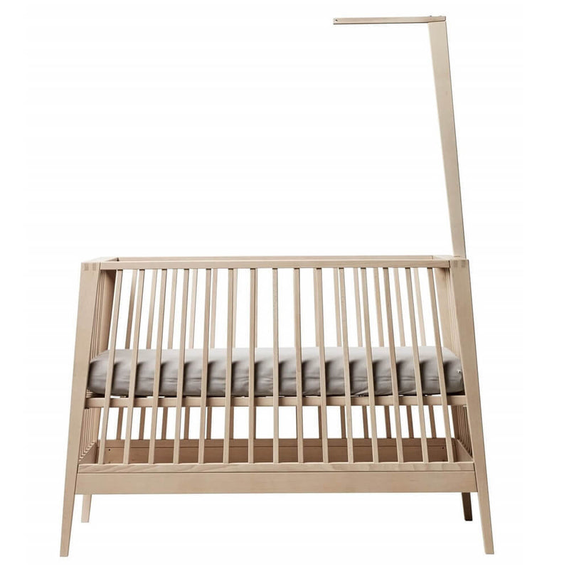 The Leander Linea/Luna Cot Canopy Rod by Leander is a minimalist accessory, crafted from solid beech with a light finish, featuring vertical slats and an attached tall canopy rod extending above one end. A thin mattress is included inside.