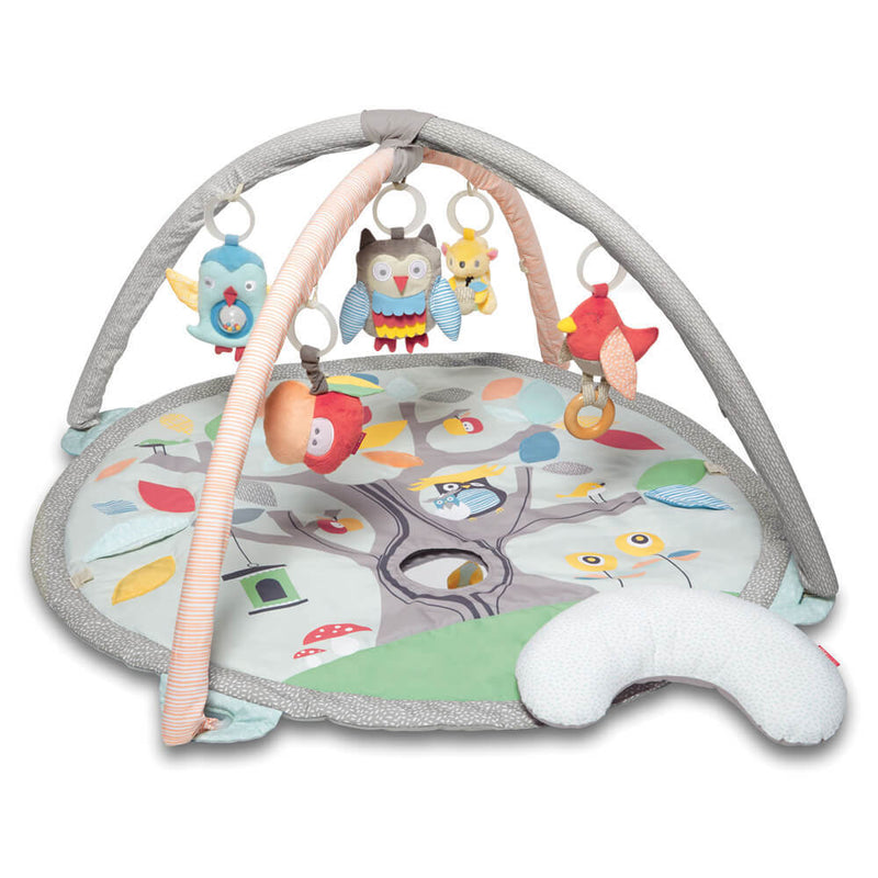 The Skip Hop Activity Gym Treetop Friends Grey Pastel features a soft mat with tree and owl designs, four arches with plush toys (owl, fox, bird) for multi-sensory play, and includes a small Tummy Time pillow.