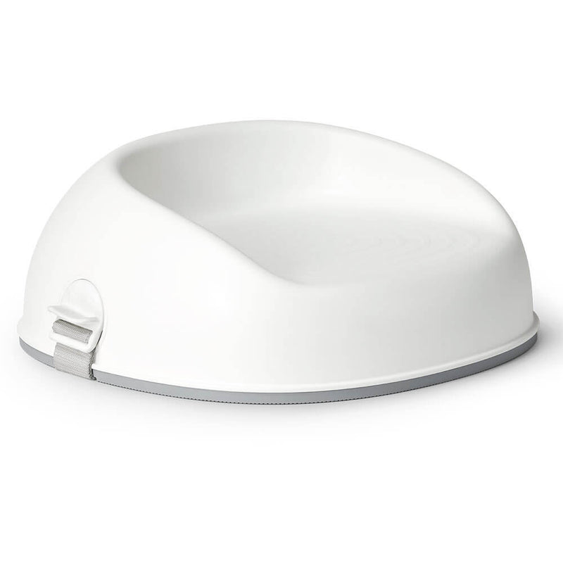 The BabyBjorn Booster Seat by BabyBjorn is a white plastic seat with a rounded backrest and side safety strap, designed to be placed on a chair for young children.