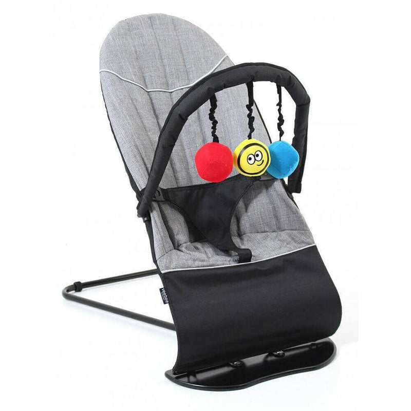 The Vee Bee Minder Bouncer Quilted is a gray baby bouncer by Vee Bee with a black frame and seat, plus a toy bar featuring three hanging soft balls: one red, one blue, and one yellow with a smiley face.