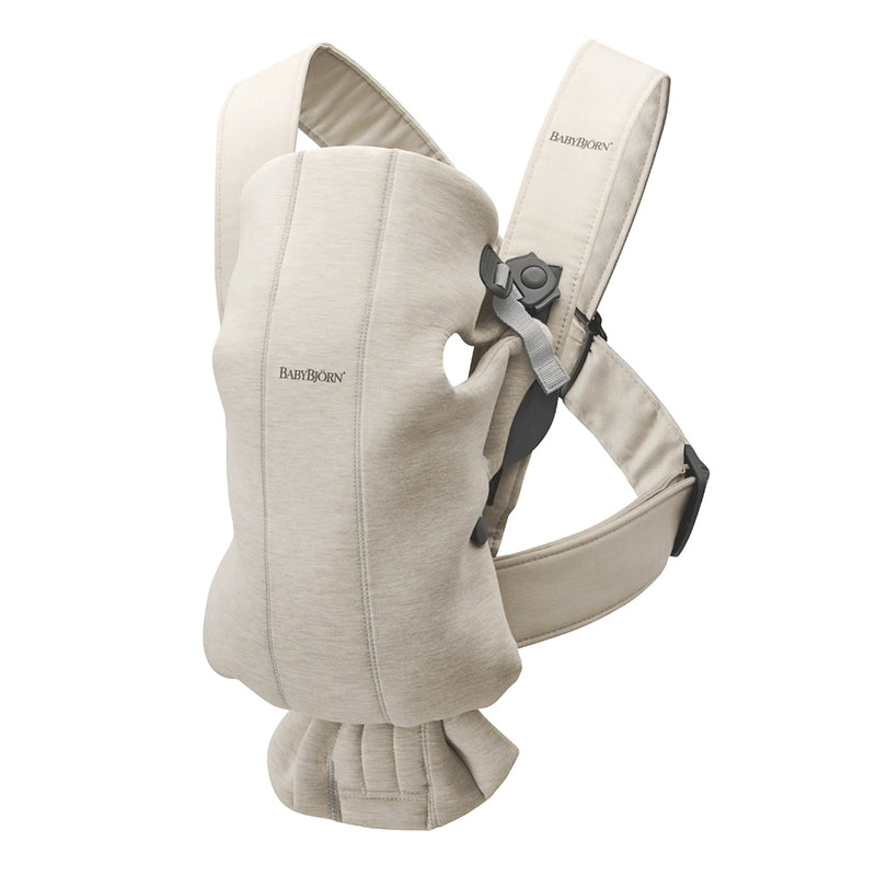 The BabyBjorn Carrier Mini 3D Jersey is a beige newborn carrier with adjustable padded straps and secure buckles, designed to hold your infant close to your chest in soft, comfortable 3D Jersey fabric.