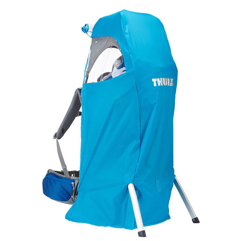 The Thule Sapling Child Carrier Rain Cover is a bright blue rain cover by Thule, designed to shelter the seating area. It features a packable design, stands upright on metal frame legs, and includes an attached storage pouch at the bottom.