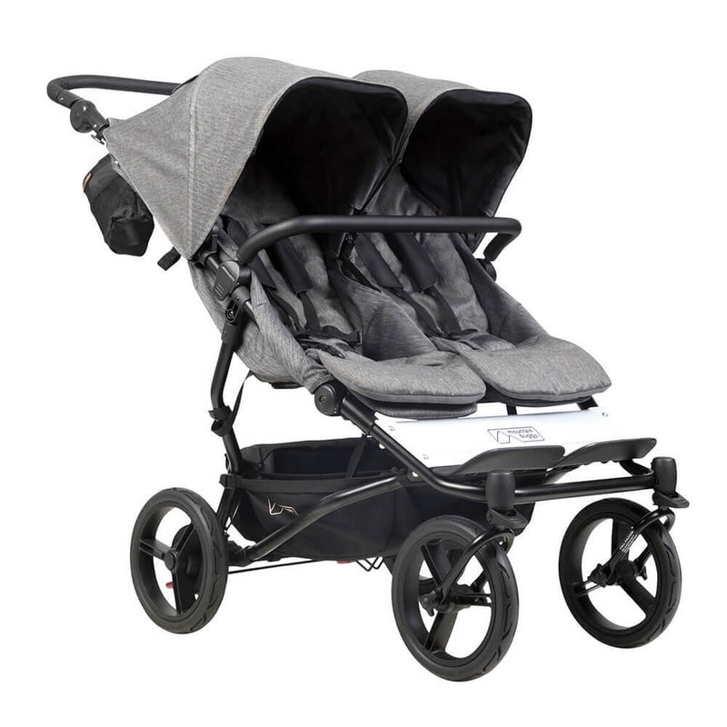 The Mountain Buggy Duet V3 Luxury Herringbone by Mountain Buggy features two side-by-side seats with canopies, a black frame, four large wheels, stylish gray herringbone fabric, and a storage basket—perfect for parents on the go.
