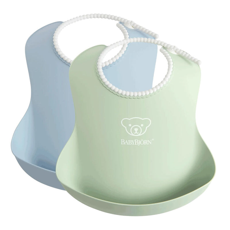 The BabyBjorn Bib 2-Pack includes a light blue and a light green adjustable bib, each with a white beaded neck strap. The green bib features the BabyBjorn bear logo and brand name printed on it.