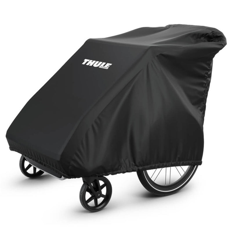 A Thule Chariot Storage Cover, in black and made from durable fabric, is placed over a two-wheeled bike trailer, covering the trailer except for its wheels.