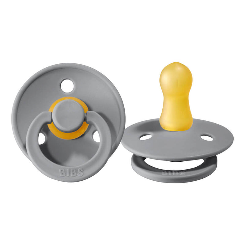 Two gray Bibs Dummies BIBS Colour Dummies 2pk pacifiers with round natural rubber nipples: one is shown front-on, displaying the shield and ring handle; the other is side-on, highlighting the nipple shape.