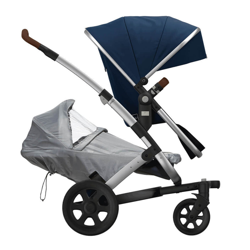 The Joolz Geo Raincover for Lower Seat by Joolz protects the lower seat of your modern stroller with a blue sun canopy, black frame, and large black wheels, using a water-repellent cover for excellent weather protection.