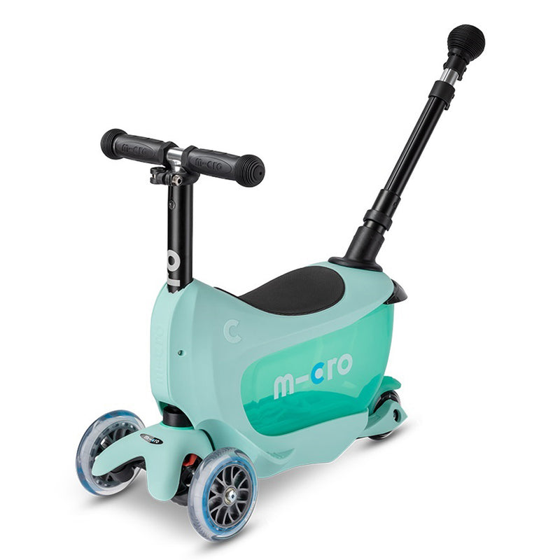 The Micro Mini2Go Deluxe Plus is a light blue three-wheel toddler scooter with a seat, black adjustable handlebars, pull handle, "m-cro" branding on the side, and a convenient storage compartment under the seat.