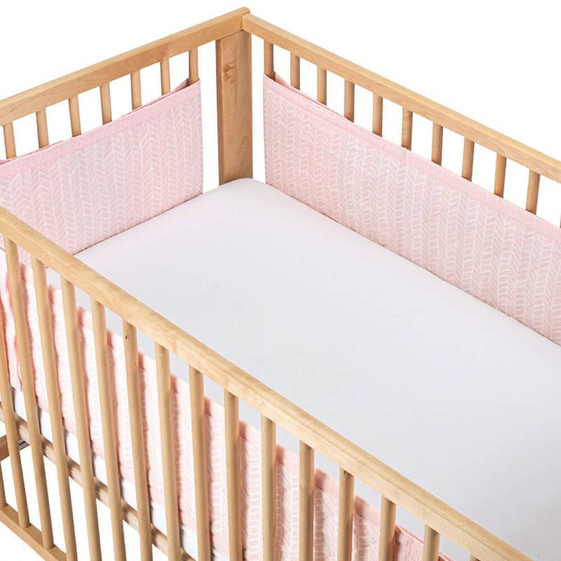A wooden baby crib with a plain white mattress and the Airwrap Cot Liner Muslin 4 Sides from Airwrap in light pink pattern, offering breathable, safe protection with vertical wooden slats as a stylish alternative to traditional cot bumpers.