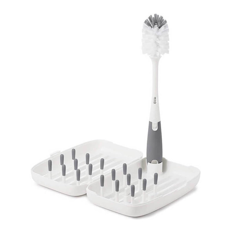 The Oxo Tot On-The-Go Drying Rack & Bottle Brush features a white and gray brush standing upright among gray pegs in the open rack—an essential, portable cleaning solution from Oxo Tot for baby bottles while traveling.