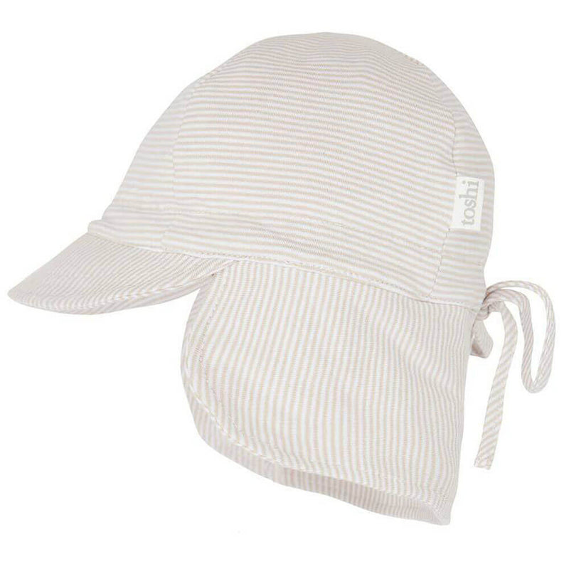 The Toshi Flap Cap is a light-colored, striped baby hat featuring a long neck flap and back tie for sun protection, extra neck coverage, and comfort. Made of soft, lightweight fabric with a small "Toshi" tag on the side.