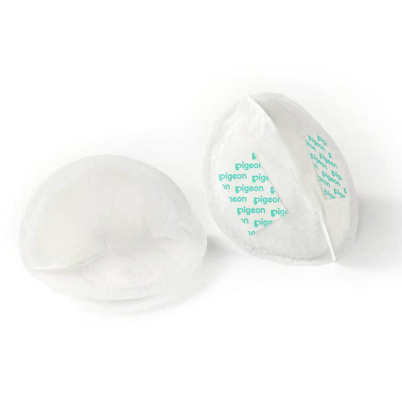Two white Pigeon ComfyFEEL Breast Pads from a 50pk are shown—one flat, one upright—both ultra-soft with a curved shape and the word "pigeon" in green printed on the inner surface.