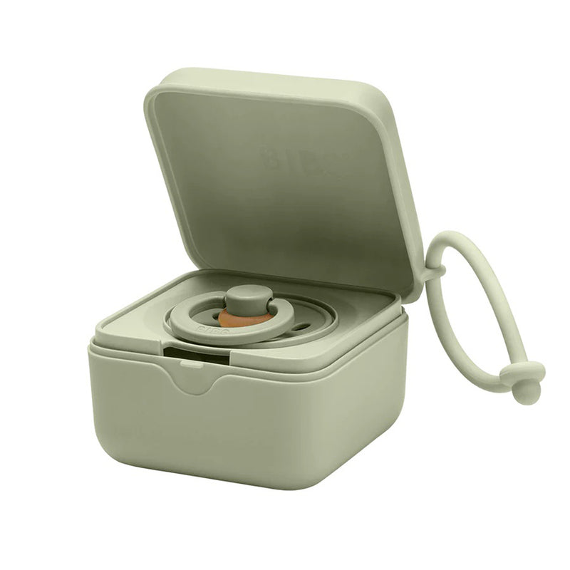 The BIBS Pacifier Box by Bibs Dummies is a small, light green container with a hinged lid, revealing a circular collapsible cup and an attached looped strap—perfect for storing or sterilising your pacifier on the go.