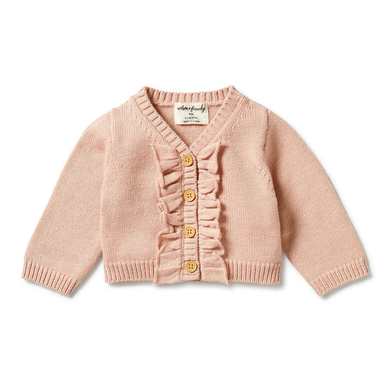 The Wilson & Frenchy Knitted Ruffle Cardigan Rose is a light pink long-sleeve cardigan with ribbed cuffs and hem, wooden front buttons, and delicate ruffle detailing along the button placket.