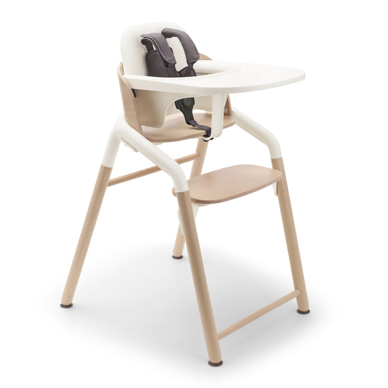 The Bugaboo Giraffe High Chair Complete by Bugaboo features light wood legs, a white seat and tray, beige accents, an ergonomic baby seat, adjustable footrest, and a dark gray safety harness.