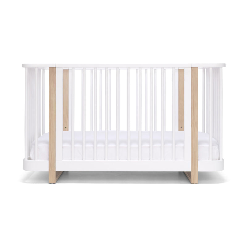 The Seena Pisa Cot by Seena features white slats, light wood accents, a non-toxic design, and a white mattress—shown front view—making it the perfect sustainable nursery furniture choice.