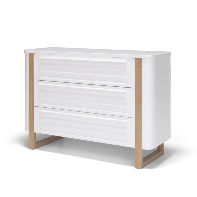 The Seena Pisa 3 Drawer Chest by Seena features three white drawers, light wood legs and trim, grooved fronts, and non-toxic finishes—a sleek, minimalist dresser ideal as sustainable nursery furniture.