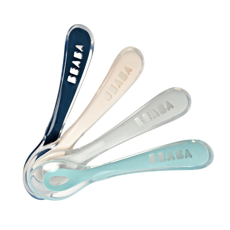 The Beaba 2nd Stage Soft Silicone Spoons 4 Pack includes gum-friendly baby spoons in dark blue, light pink, light gray, and light teal, each with “BEABA” engraved and transparent handles for gentle feeding.