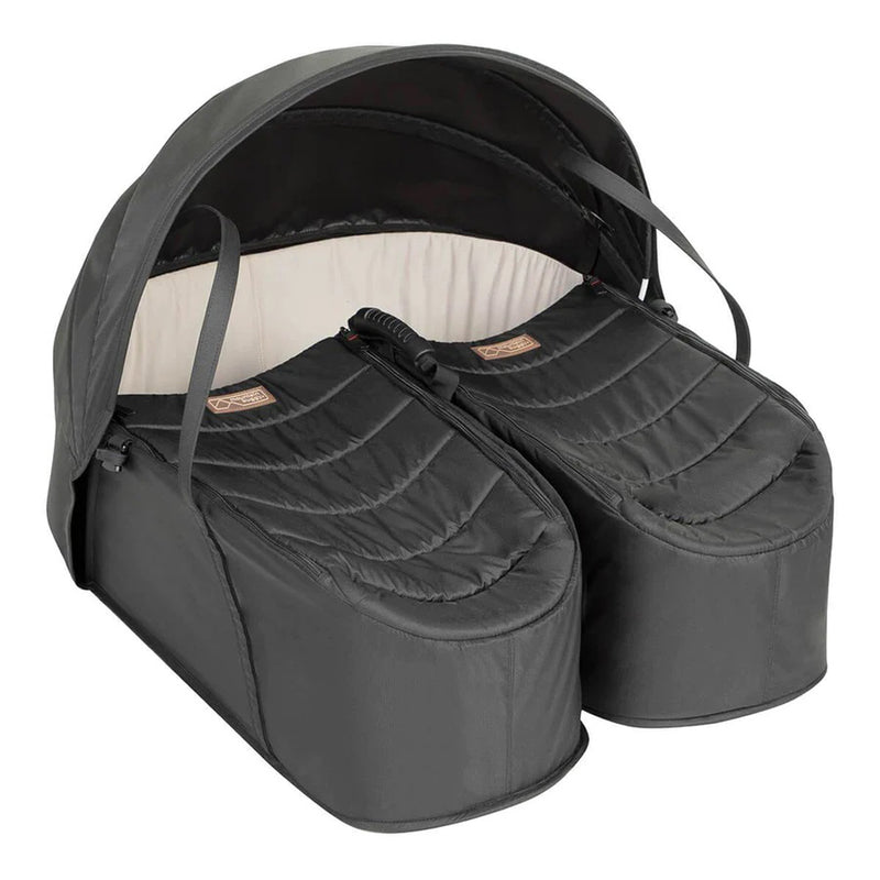 The Mountain Buggy Cocoon For Twins by Mountain Buggy is a black, lightweight twin bassinet with padded interiors, folding canopy, individual zippered covers, and soft light-colored linings for cozy newborn sleep side by side.