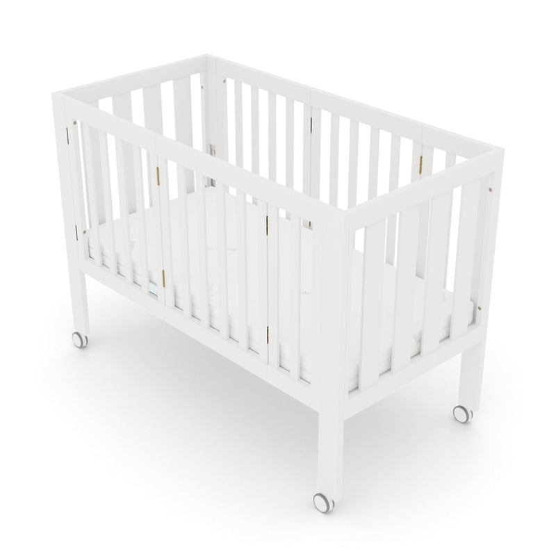 The BabyRest Dixie by BabyRest is a compact white wooden crib with vertical slats, a flat mattress, and four small wheels for easy mobility.