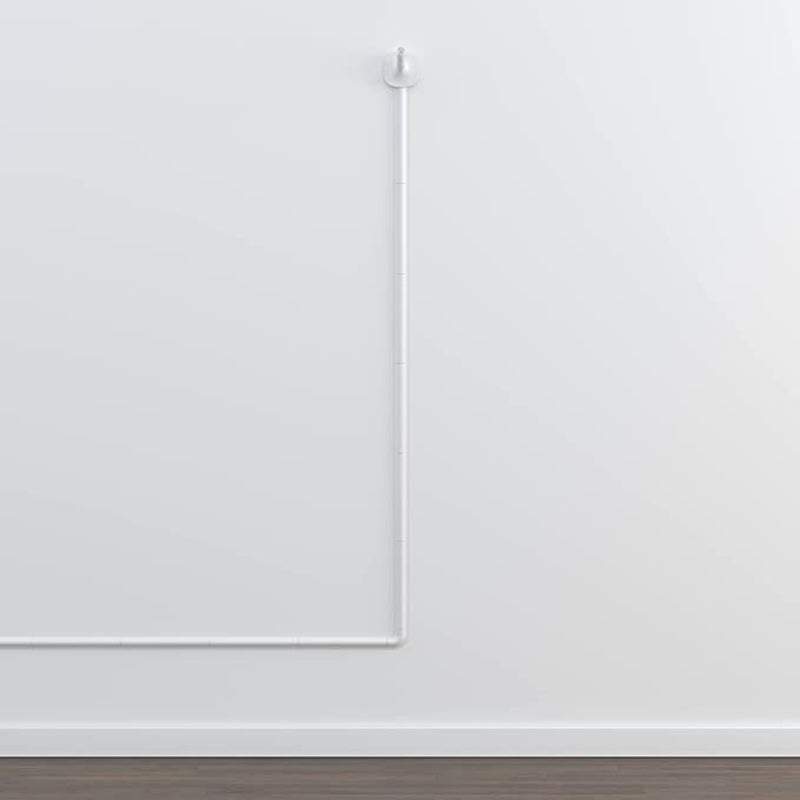 The Nanit Wall Mount Replacement N315AU by Nanit is installed high on a white wall, viewed from above, with its cord extending straight down and then running horizontally near the dark wood floor.