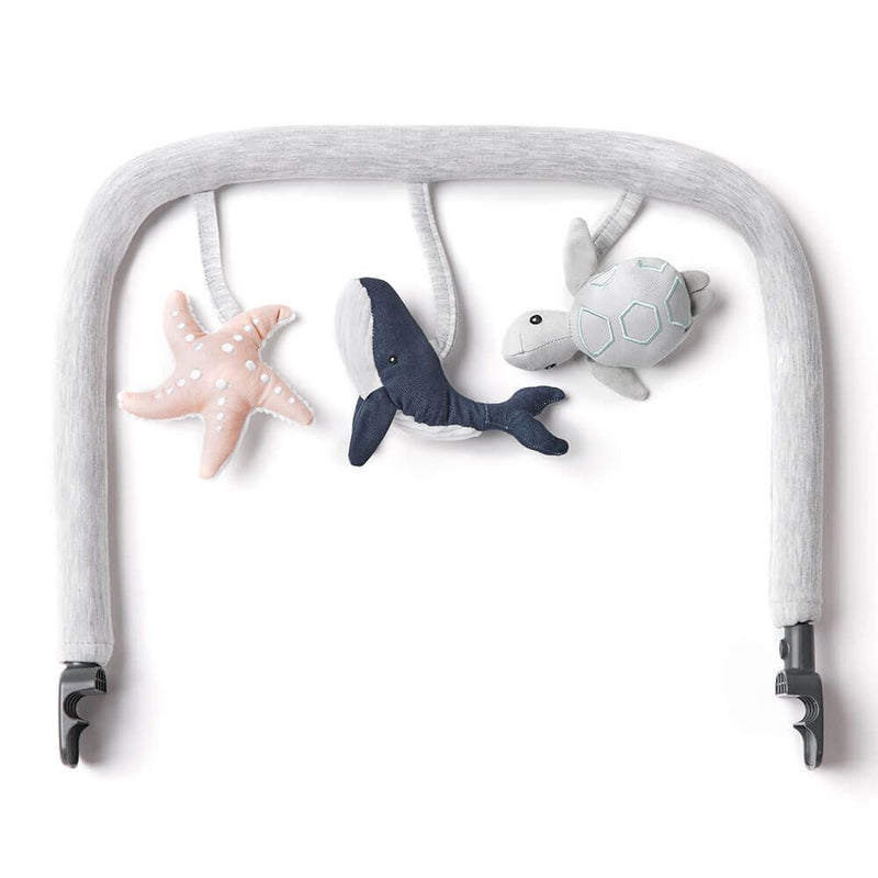 The ErgoBaby Evolve 3 in 1 Bouncer Toy Bar Ocean Wonders is a soft gray stroller arch with three plush ocean animals—a pink starfish, blue whale, and gray turtle—attached by spiral loops. Ideal for the Evolve 3-in-1 Bouncer or stroller.