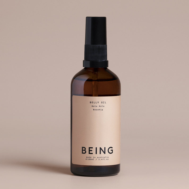 A brown glass bottle with a black pump, labeled "Being Skincare Belly Oil," is formulated with gotu kola and rosehip by Being Skincare to help reduce stretch marks during pregnancy. It rests on a neutral beige background.