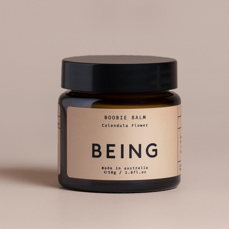 A small brown 50g glass jar with a black lid labeled "Being Skincare Boobie Balm." This Australian-made postpartum balm soothes nipples, and is shown against a neutral background.