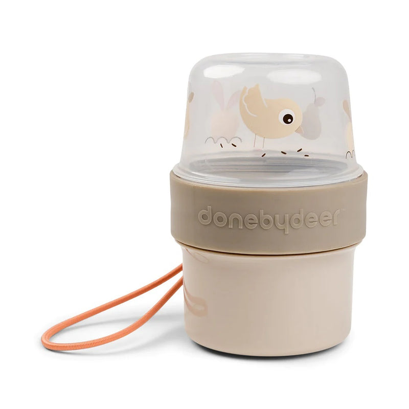 The Done By Deer To Go 2-Way Snack Container Birdee Sand features a beige and tan design with bird illustrations on the lid, an orange carrying strap, and "done by deer" logo on the side.