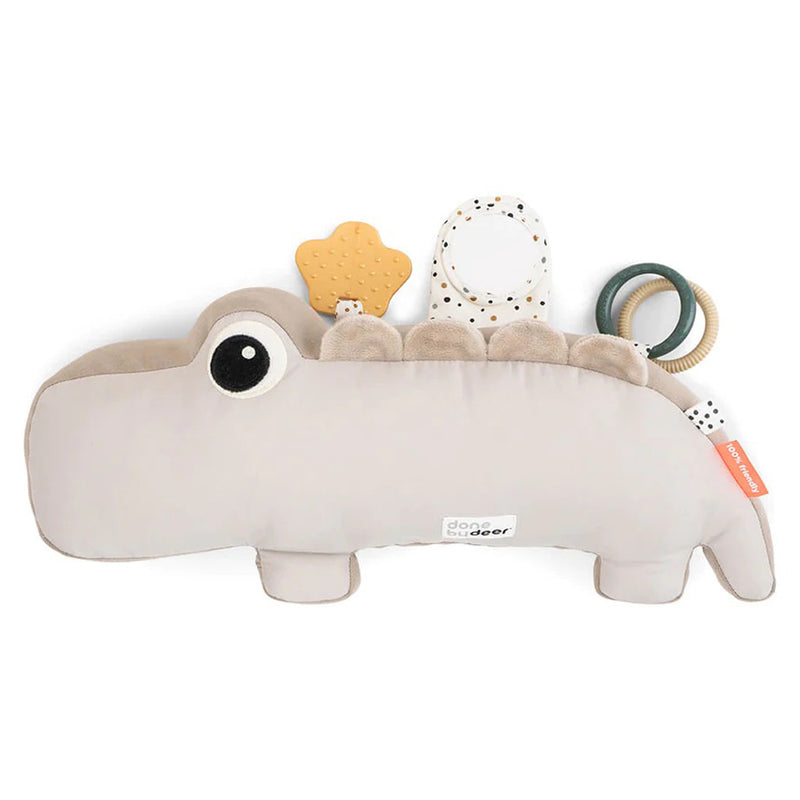 The Done By Deer Tummy Time Activity Toy Croco Sand is a soft, light gray dinosaur-shaped sensory toy with a mirror, teether, fabric tag, large eye, and two ring rattles—perfect as a tummy time pillow and baby activity toy.