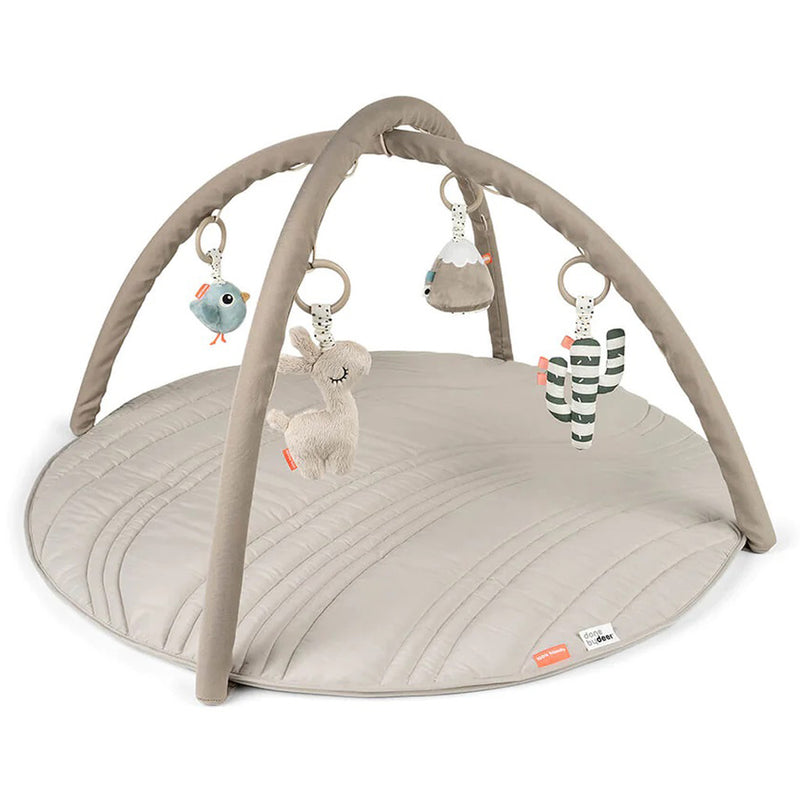 The Done By Deer Activity Play Mat Lalee Sand is a neutral-colored round mat with two crossed arches and four soft sensory toys: bird, llama, mountain, and cactus. Brand: Done By Deer.