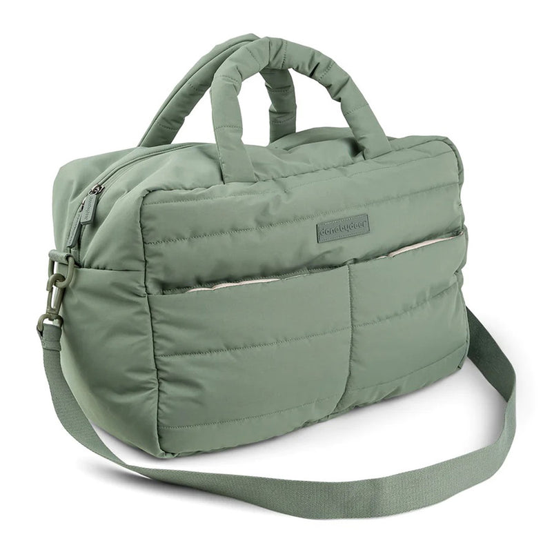 The Done By Deer Quilted Changing Bag Green is made from recycled polyester and features two short handles, an adjustable shoulder strap, two front pockets, a zippered main compartment, and a soft quilted design.