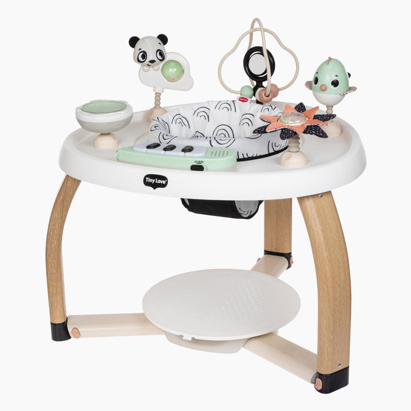 The Tiny Love 5-In-1 Here I Grow Stationary Activity Centre features wooden legs, a white circular tabletop, sensory toys like a panda and bird, spinning elements, and a patterned fabric seat to support baby development.