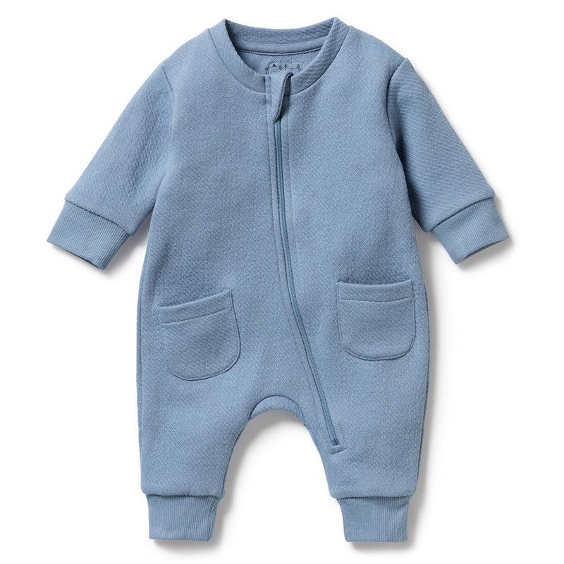 The Wilson & Frenchy Storm Blue Organic Quilted Growsuit features long sleeves, two front pockets, ribbed cuffs, and a diagonal zipper. Made from GOTS-certified organic cotton for softness and peace of mind.