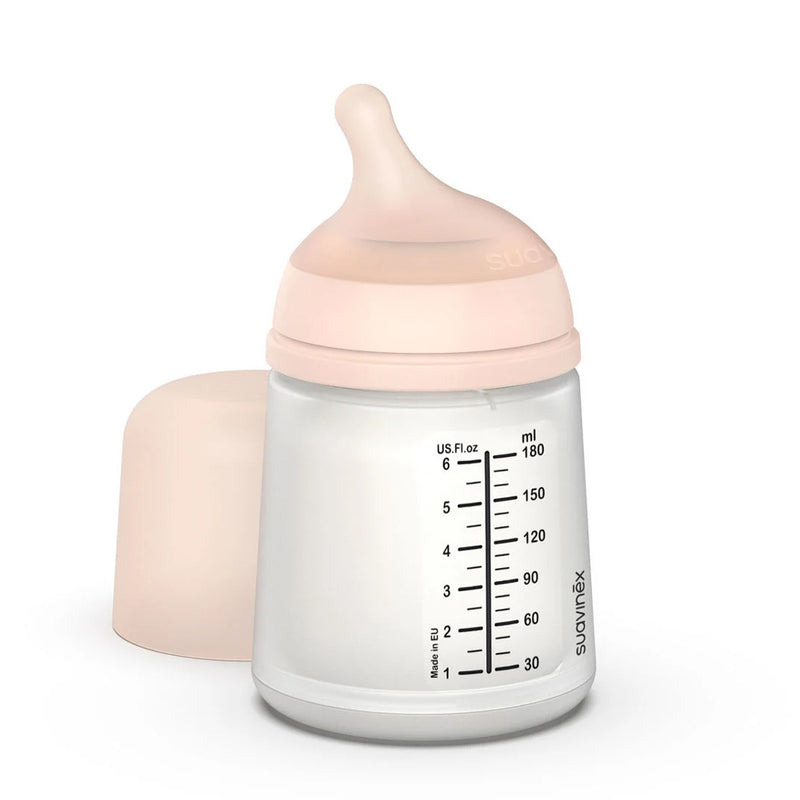 The Suavinex Zero Zero Anti Colic Bottle 180ml Slow Flow 0M+ features a soft pink cap, silicone nipple, and ml/oz markings—perfect for breastfeeding or formula feeding. Cap shown beside bottle. Brand: Suavinex.