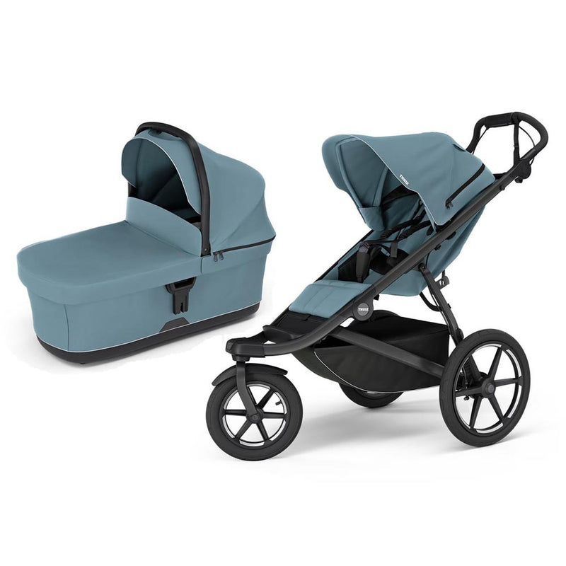 The Thule Urban Glide 3 Stroller + Bassinet in Mid Blue features a matching blue bassinet, a black frame, large all-terrain wheels, and an under-seat storage basket—ideal for parents wanting style and versatility.