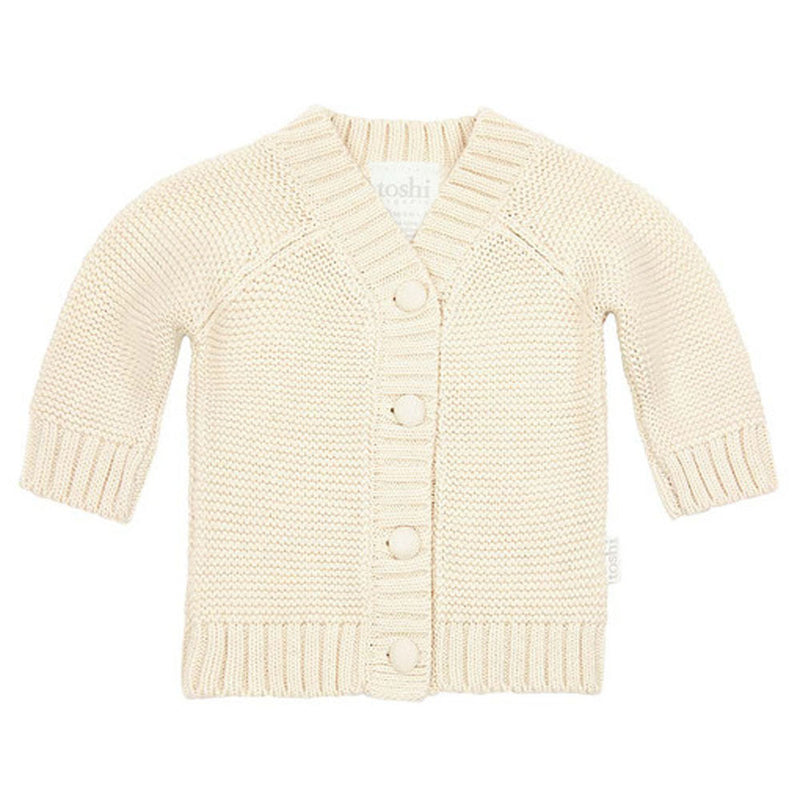 The Toshi Organic Cardigan Andy/Feather is a cream-colored organic cotton baby sweater with long sleeves, a V-neck, ribbed cuffs and hem, four large front buttons, and an all-over visible knit texture.