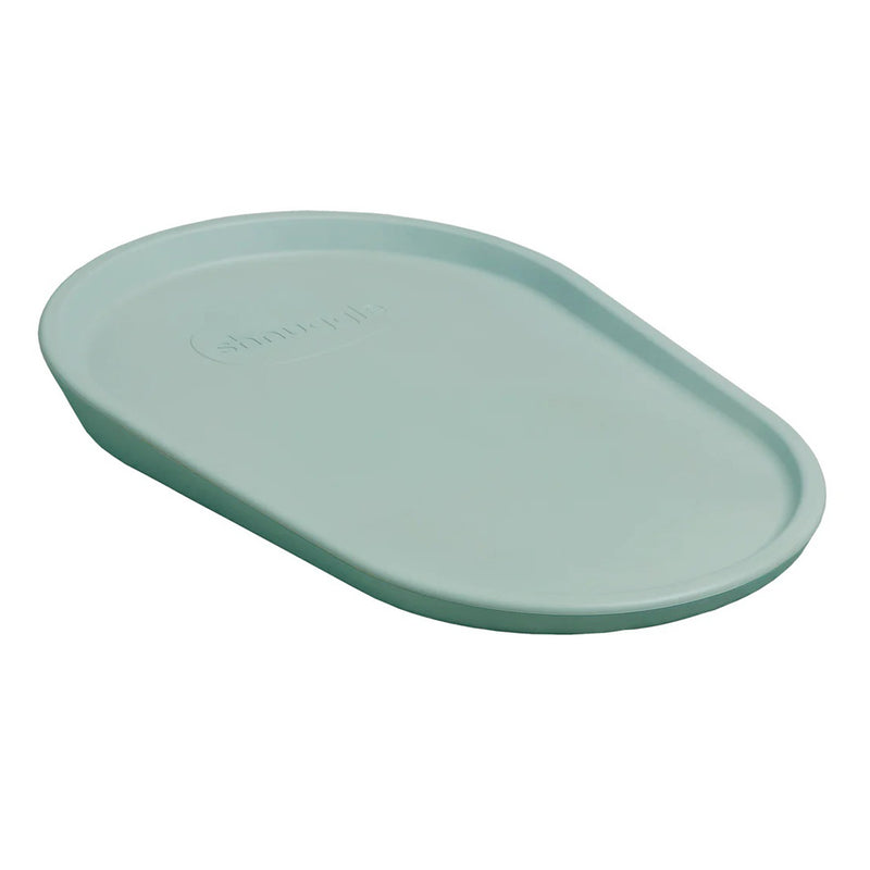 The Shnuggle Squishy Change Mat Eucalyptus by Shnuggle is an oval silicone mat in light blue-green with raised edges and a smooth, waterproof surface, shown angled against a white background.
