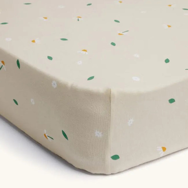 The ErgoPouch 2 In 1 Waterproof Fitted Sheet Cot Daisy Sprinkle features a beige floral print with white flowers and green leaves, made from organic cotton for safe baby sleep, and fits snugly on the mattress.