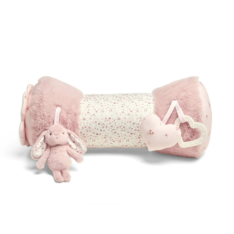The Mamas & Papas Tummy Time Roll Pink is a soft, cylindrical cushion with plush pink ends, a floral-patterned center, and toy charms (a bunny and two hearts) that encourage sensory development during play.