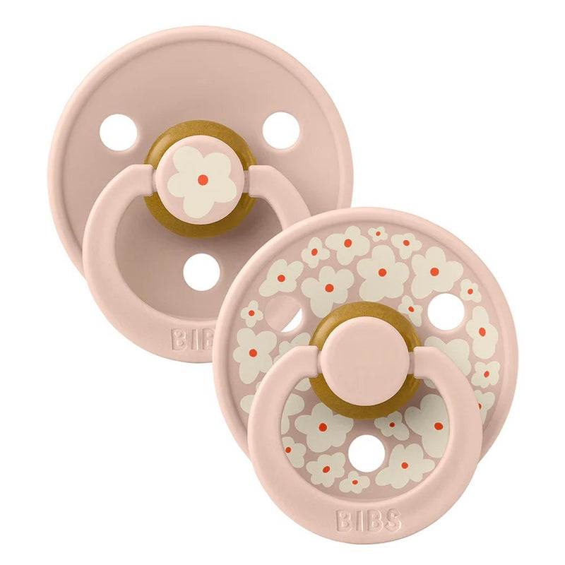 The Bibs Dummies Studio Colour Jasmine Blush Mix by Bibs Dummies includes two pink dummies: one with white and orange flowers, one plain with a single flower—both have natural rubber latex nipples, ring handles, and "BIBS" branding.