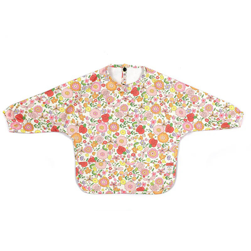 The IZIMINI Paloma Bib is a long-sleeved, waterproof baby bib with a vibrant floral pattern in pink, yellow, orange, and green. Shown flat with arms outstretched, it's ideal for toddlers at mealtimes to keep clothes clean.