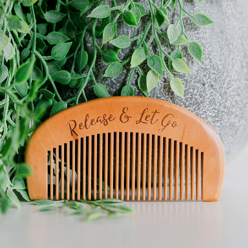 Partum Panties The Labour Comb by Partum Panties, engraved with "Release & Let Go," sits before a leafy green plant and gray pot, offering pain relief during labour.