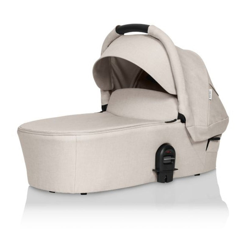 The Britax Safe-N-Sound Mini Bassinet in beige features a canopy, black handle, and attaches to the Britax Mini Stroller. This lie-flat bassinet offers a sleek, modern look and is shown on a white background.