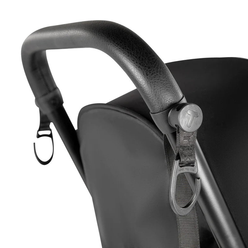 Close-up of a black stroller handle with textured grip, featuring SmarTrike Clips—one metal and one plastic—for hanging bags or accessories. These practical SmarTrike stroller accessories make outings easier, with the stroller fabric also visible.
