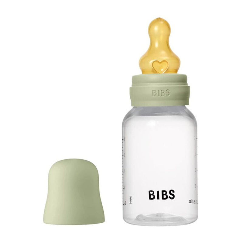 The Bibs Dummies Latex Baby Bottle 150ml features a clear, dishwasher-safe bottle with measurement marks, a soft green lid and cap, and a yellow breast-like nipple for easy feeding and cleaning.